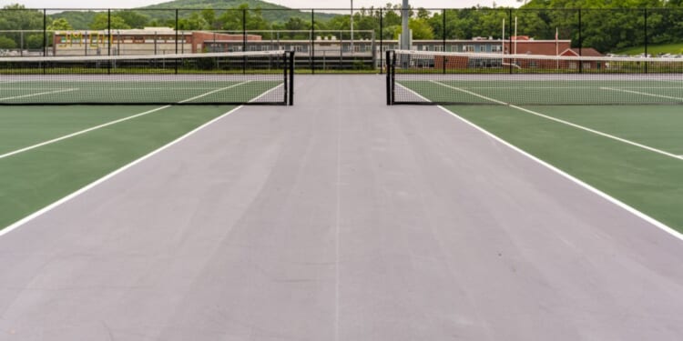 A new green tennis court with white lines and gray outside of the play area.