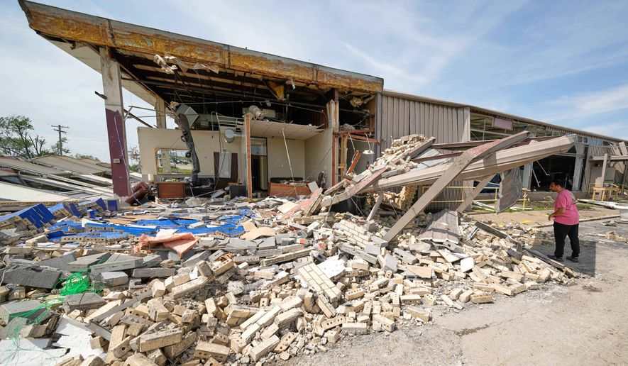 A man looks though debris Tuesday, April 14, 2026, at a pipe manufacturing facility that was damaged by a tornado Monday in Ottawa, Kan. (AP Photo/Charlie Riedel)