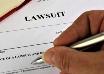 A man's hand readies a pen to begin filling out a lawsuit.