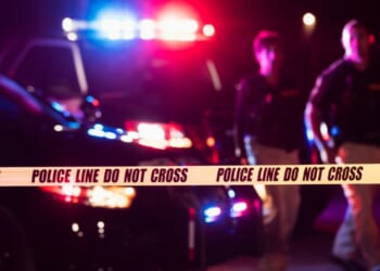 Two police officers walk in front of flashing patrol cars at a crime scene.