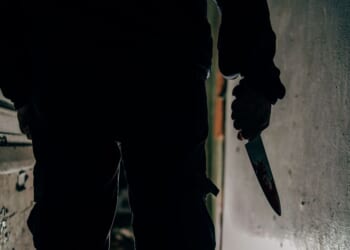A murderer holds a bloodstained knife.