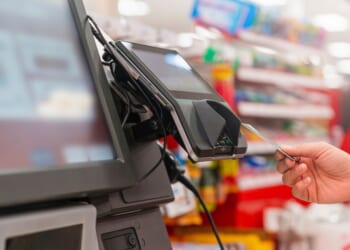 A person uses a card to pay at a grocery store self-service kiosk.