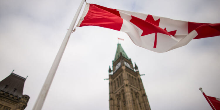 Low angle shot of the Canadian flag with tall, narrow building behind it.