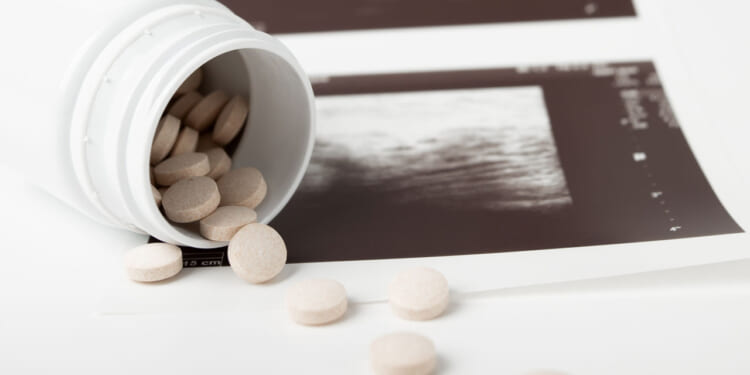Pills spill out of a white bottle onto the edge of an ultrasound.