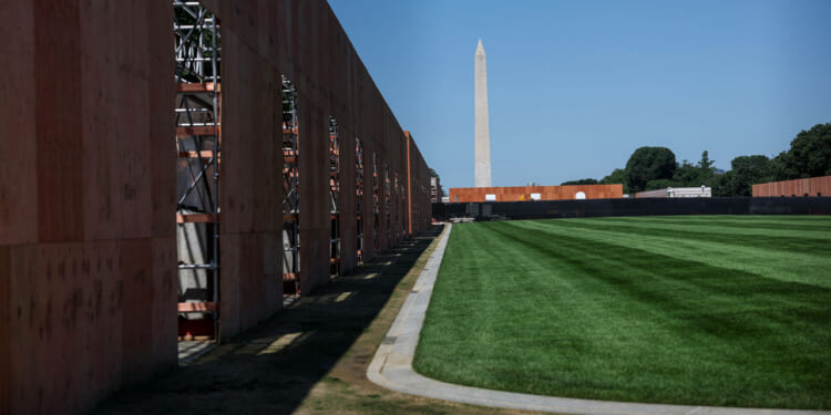 A temporary wooden fence surrounds a section of the National Mall, with the Washington Monument in the background.