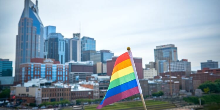 A rainbow flag flies in the foreground with the city of Nashville in the background.