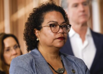 California Assemblymember Mia Bonta looks on as Gov. Gavin Newsom stands in the background.