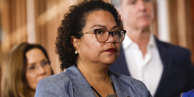 California Assemblymember Mia Bonta looks on as Gov. Gavin Newsom stands in the background.