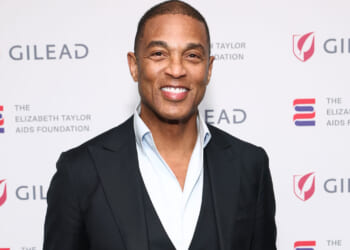 Former CNN host Don Lemon in black jacket and open white shirt stands against a white background at Elizabeth Taylor AIDS Foundation event.