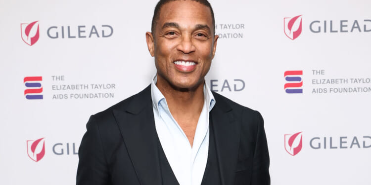 Former CNN host Don Lemon in black jacket and open white shirt stands against a white background at Elizabeth Taylor AIDS Foundation event.