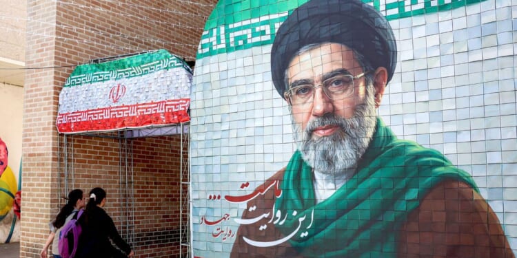 Women walk past a banner depicting Iran's current supreme leader Ayatollah Mojtaba Khamenei along a street Tehran on May 6, 2026.