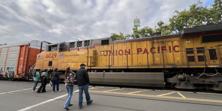 Pedestrians approach a Union Pacific freight train traveling past Jack London Square, Oakland, California, on April 26, 2026.