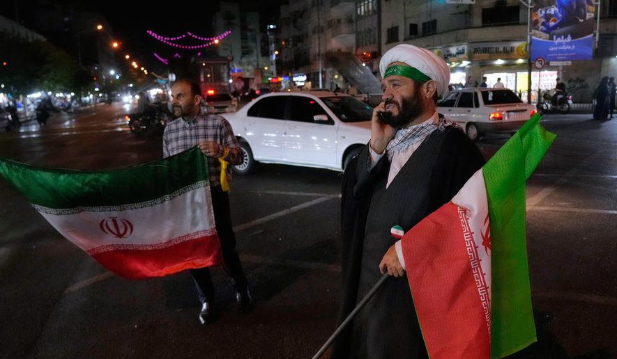 A cleric speaks on his cellphone holding an Iranian flags for a pro-government campaign in downtown Tehran, Iran, Friday, May 8, 2026. (AP Photo/Vahid Salemi)
