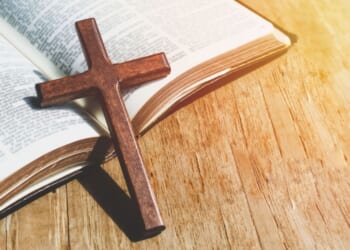 A close up of a small cross leaning against an open Bible.