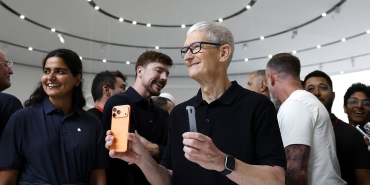 Apple CEO Tim Cook holding iPhones while surrounded by people