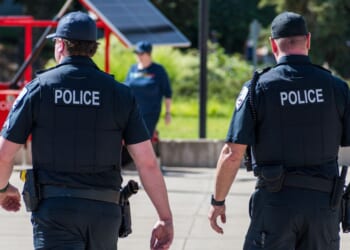 Police officers walk through a city park in the daylight.