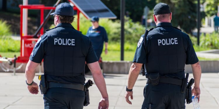 Police officers walk through a city park in the daylight.
