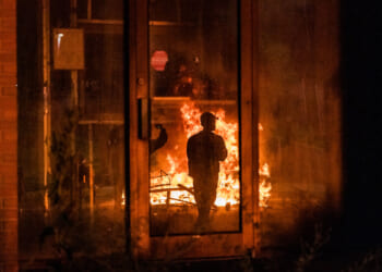 A man is silhouetted against flames at nighttime outside Newark ICE facility.