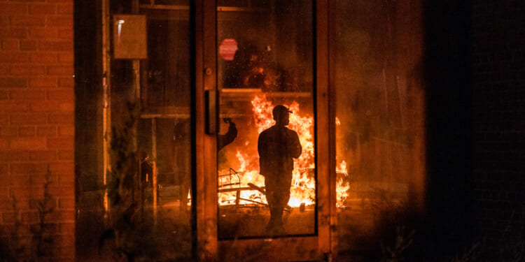 A man is silhouetted against flames at nighttime outside Newark ICE facility.