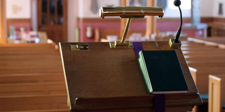 A modern wooden church pulpit with a light, microphone, and Bible on it.