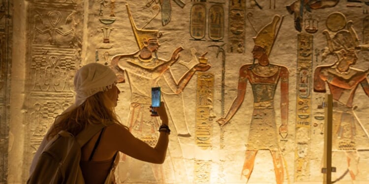 A woman holds out her smartphone and takes a picture of ancient depiction of Ramses IX at the Valley of Kings in Luxor, Egypt.