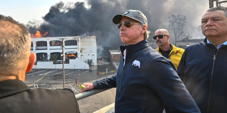 Gavin Newsom, in sunglasses and grey cap overlooks the Pacific Palisades fire.