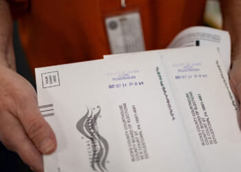 Close-up of mail-in ballots being held by a red-shirted worker.