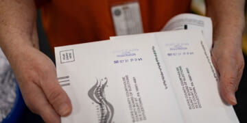 Close-up of mail-in ballots being held by a red-shirted worker.