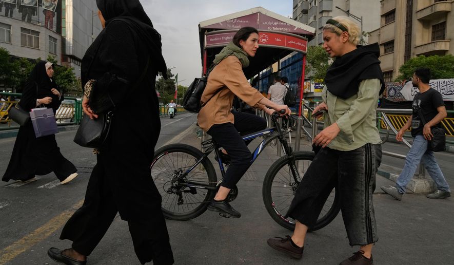 A woman rides a bicycle as others cross a street in downtown Tehran, Iran, Sunday, May 24, 2026. (AP Photo/Vahid Salemi)