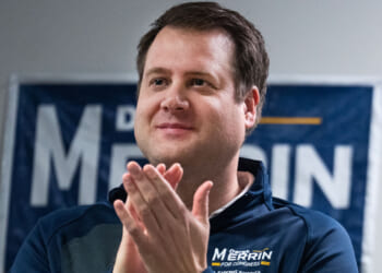 Republican Derek Merrin smiles as he applauds in front of one of his campaign signs.