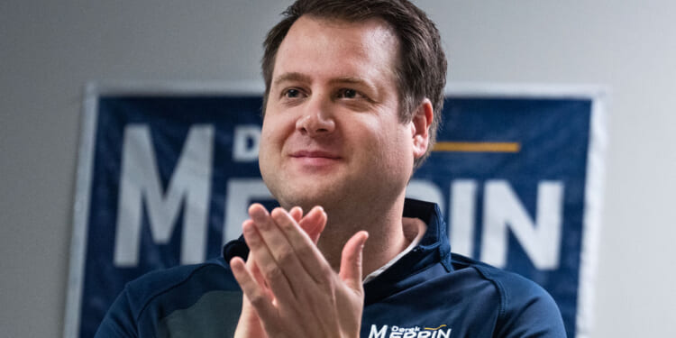 Republican Derek Merrin smiles as he applauds in front of one of his campaign signs.