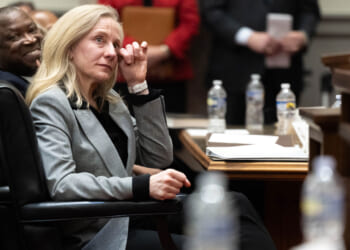 Abigail Spanberger, in a grey suit, wipes a tear from her eye while seated at a table.