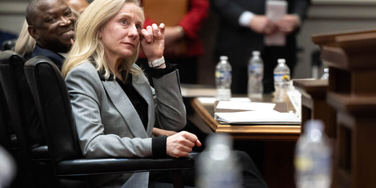 Abigail Spanberger, in a grey suit, wipes a tear from her eye while seated at a table.
