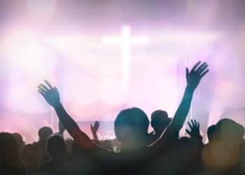Christians raising their hands in praise and worship with a cross in the background.