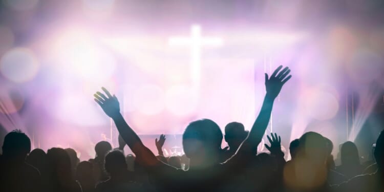 Christians raising their hands in praise and worship with a cross in the background.