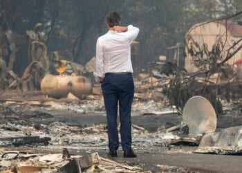 A shot from behind of Gavin Newsom, with his right hand on his neck inspecting fire devastation.