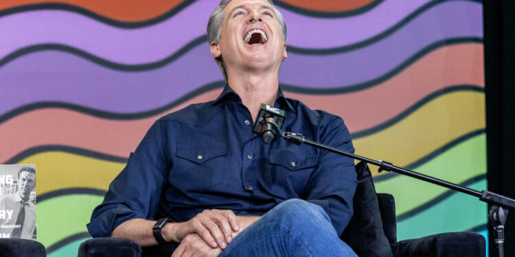 A seated Gavin Newsom with his head back laughing, in front of a backdrop of wavy rows of color.