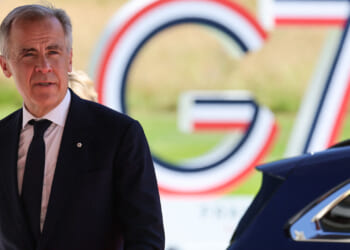 Canadian Prime Minister Mark Carney walks with G7 sign behind him.