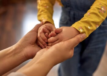 A woman holds the hands of a young child.
