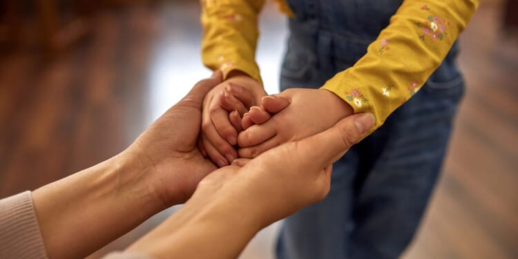 A woman holds the hands of a young child.