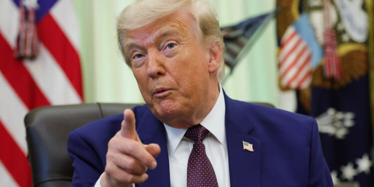 President Donald Trump gestures from his desk in the Oval Office.