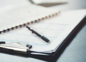 A clipboard, papers, and a pen lay on a black desk.