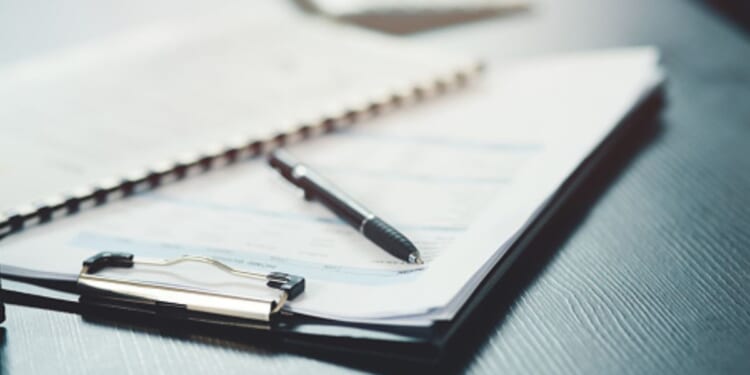 A clipboard, papers, and a pen lay on a black desk.