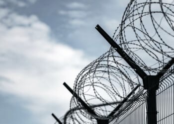 A prison with razor wire against a dark sky.