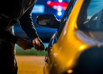 A man tries to pick a lock on a car.