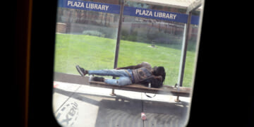 A bus window frames a person napping on the Plaza Library bench. The Kansas City Area Transportation Authority (KCATA) bus is free for all riders. (Photo by Pat Greenhouse/The Boston Globe via Getty Images)