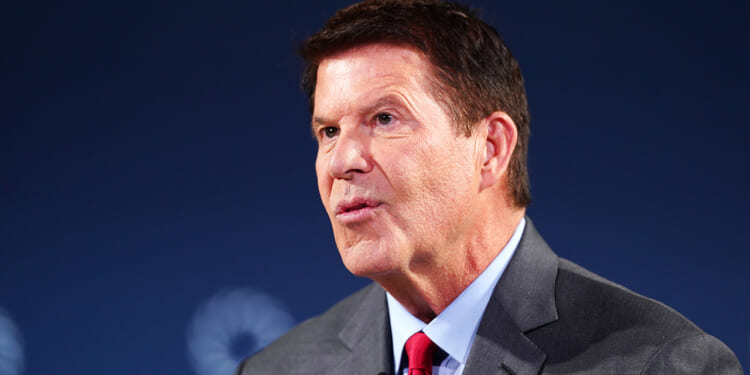Keith Krach speaking in front of a blue background.