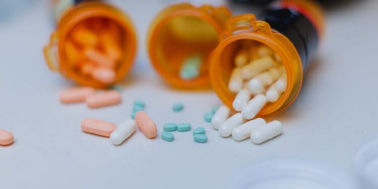 Pill bottles spill multi-colored pills out onto a white table.