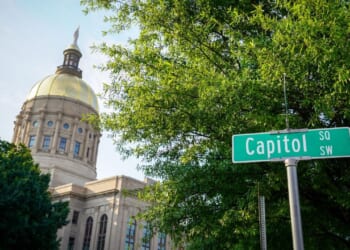 The Georgia State Capitol building is featured with trees and a street sign that says Capitol Square SW.