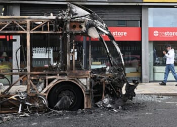 A pedestrian passes a burned-out bus Wednesday following a night of anti-immigrant riots Tuesday in Belfast, Northern Ireland.